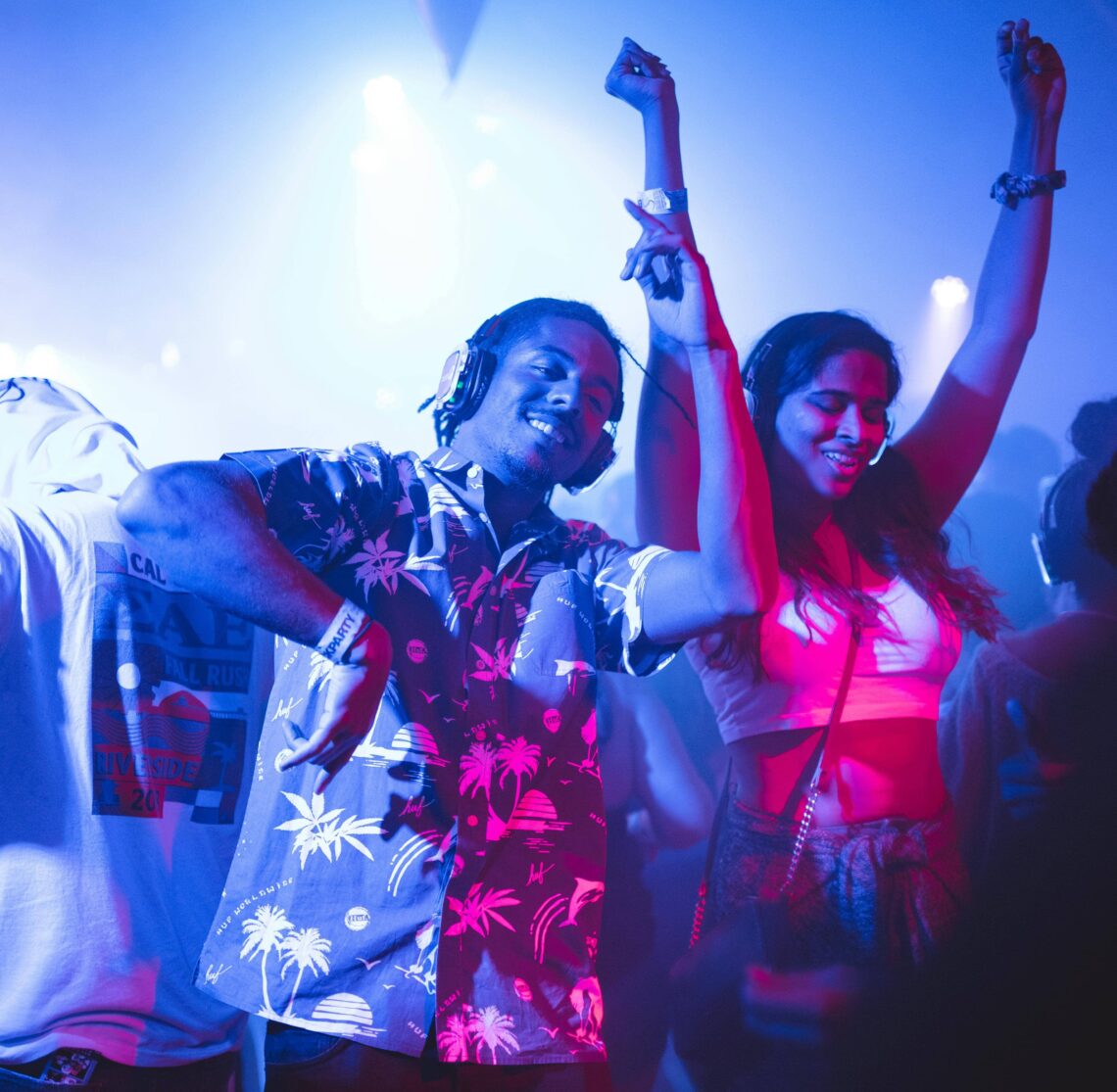 Festivals été 2025 : Deux jeunes, hommes et femmes, dansent au sons de la musique d'un dj dans une boîte de nuit sous une lumière bleue nuit.
