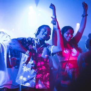 Festivals été 2025 : Deux jeunes, hommes et femmes, dansent au sons de la musique d'un dj dans une boîte de nuit sous une lumière bleue nuit.