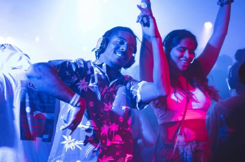 Festivals été 2025 : Deux jeunes, hommes et femmes, dansent au sons de la musique d'un dj dans une boîte de nuit sous une lumière bleue nuit.